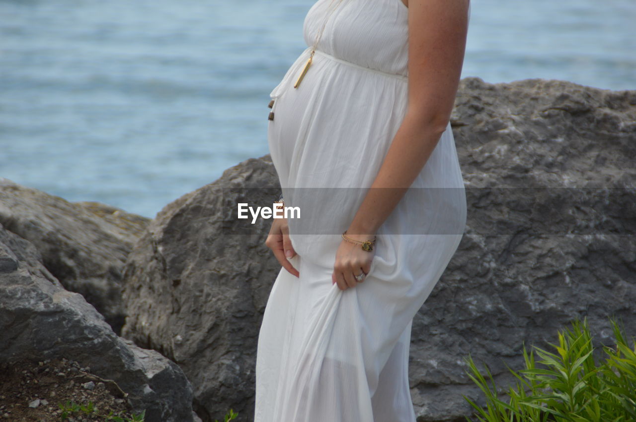 Midsection of pregnant woman standing on rock by sea