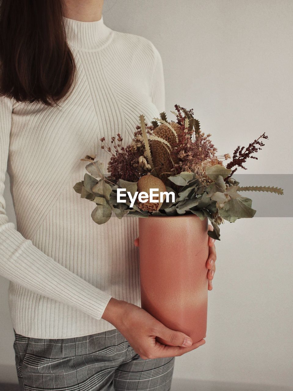 Midsection of woman holding flower bouquet against wall