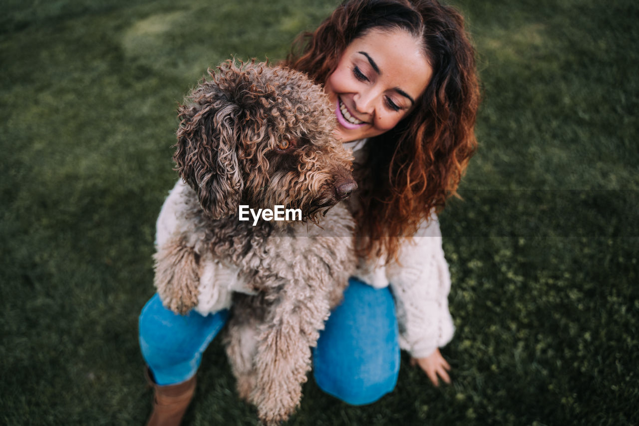 High angle view of smiling woman holding dog on grassy land