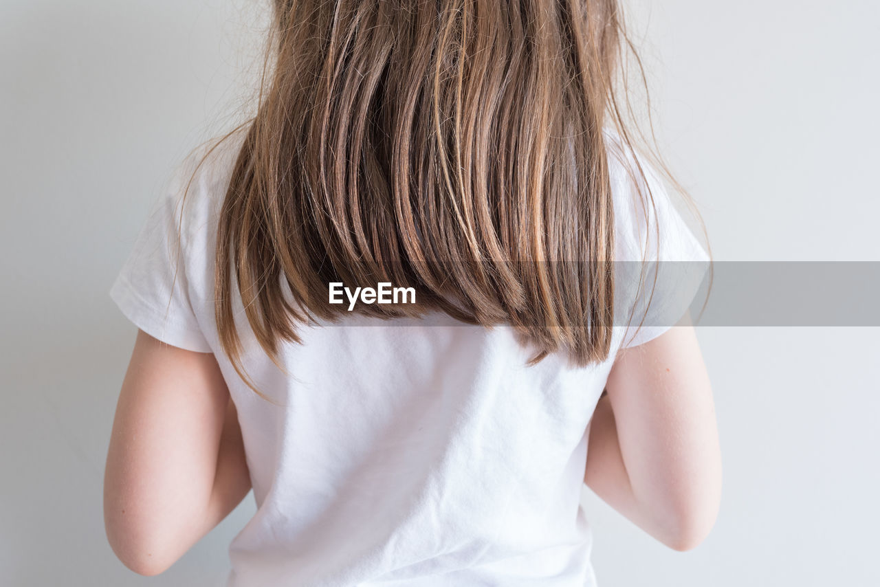 REAR VIEW OF WOMAN STANDING IN WHITE BACKGROUND