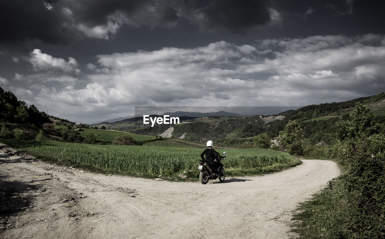 REAR VIEW OF MAN CYCLING ON ROAD