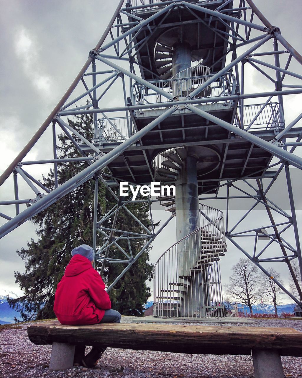 REAR VIEW OF MAN SITTING AGAINST BRIDGE