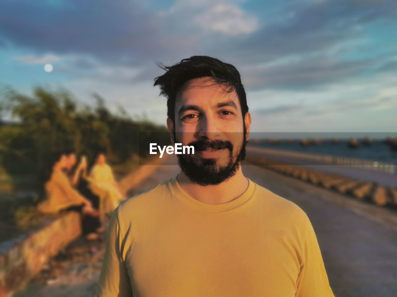 Portrait of handsome and smiling young man with facial hair standing against sky