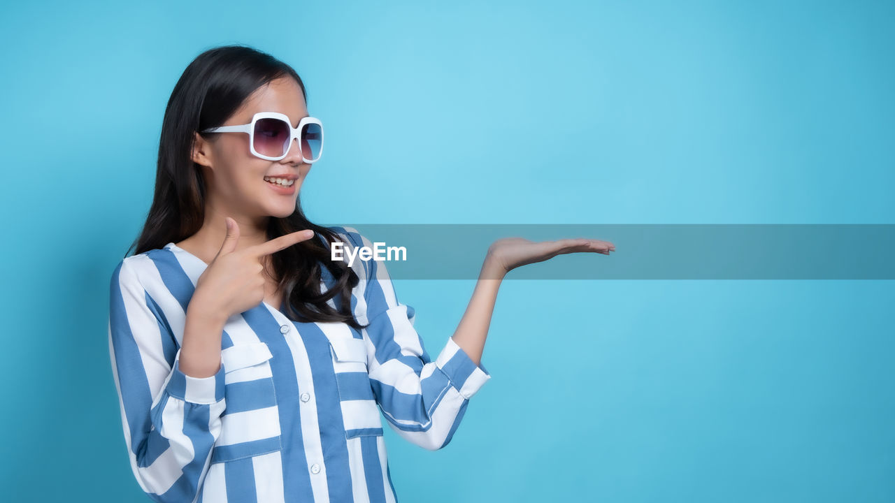 SMILING YOUNG WOMAN AGAINST BLUE BACKGROUND