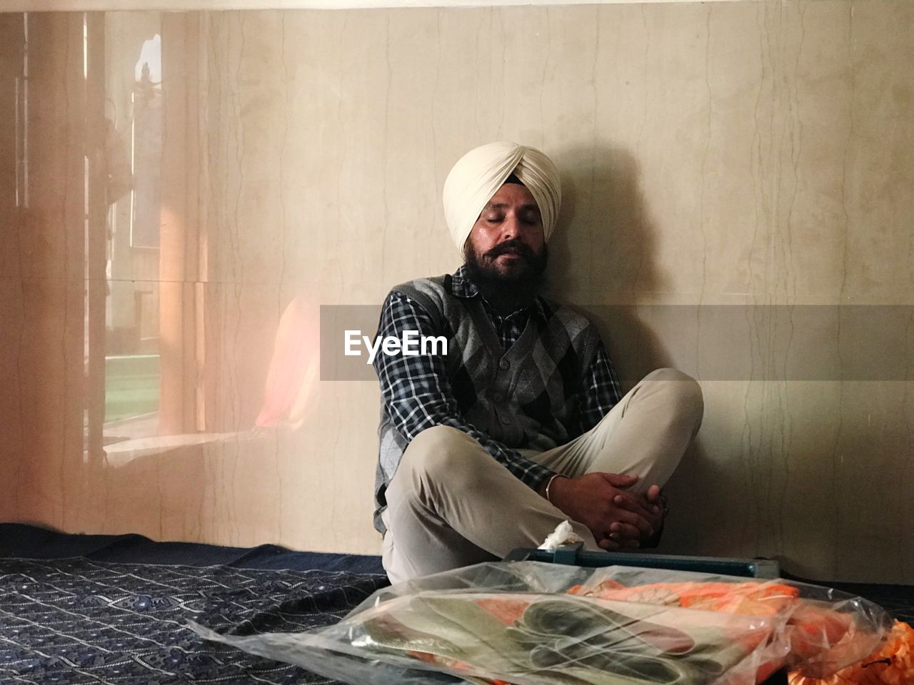 Mature man praying while sitting against wall at gurudwara