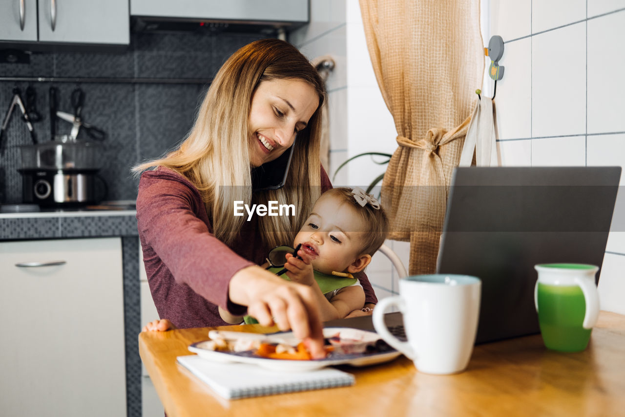 Mother feeding daughter while sitting on table at home