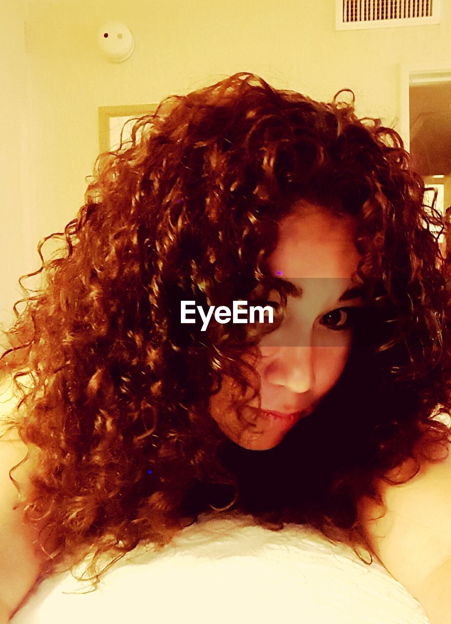 Portrait of young woman with curly brown hair lying on bed