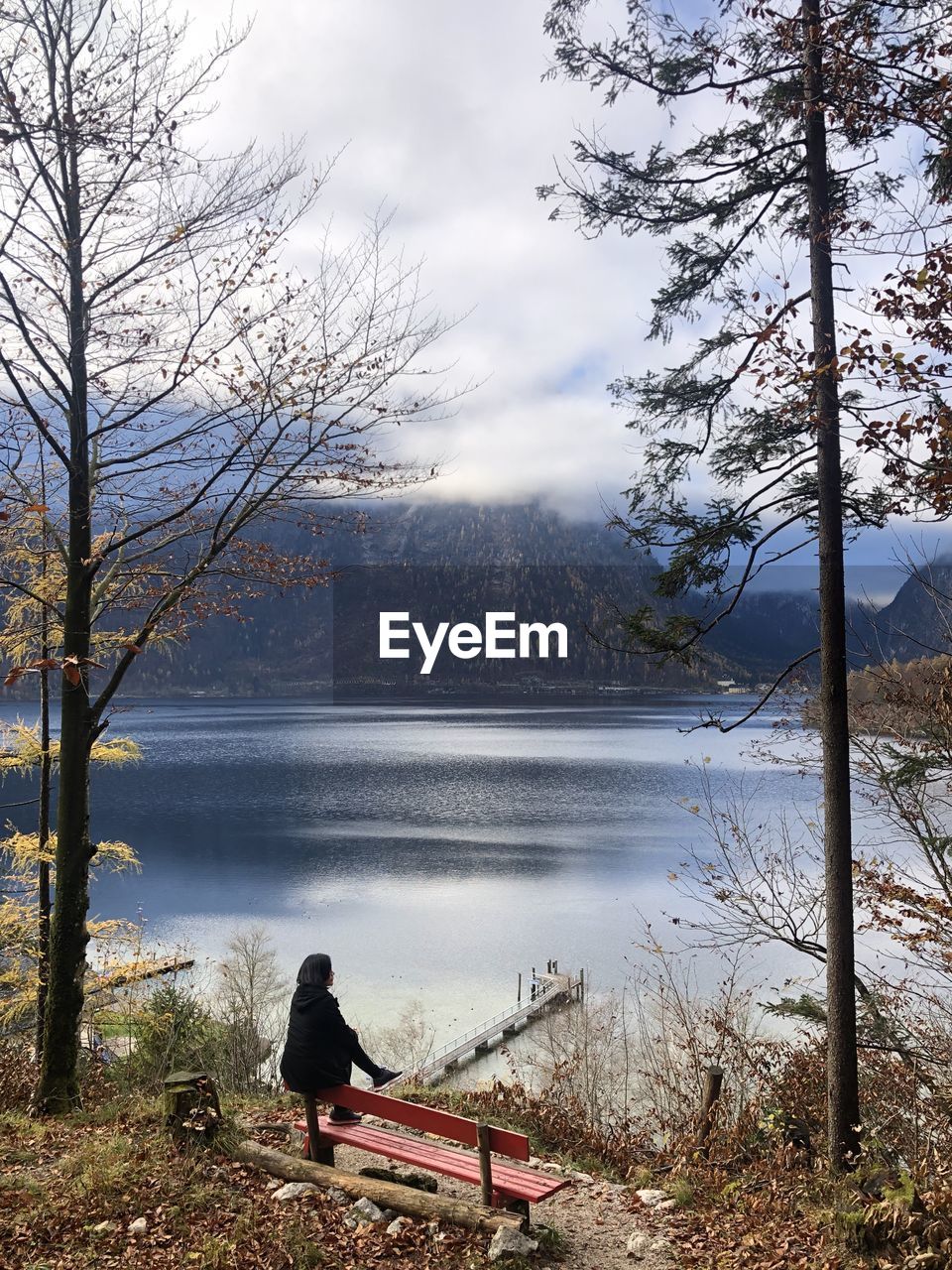 Rear view of woman sitting by lake against sky