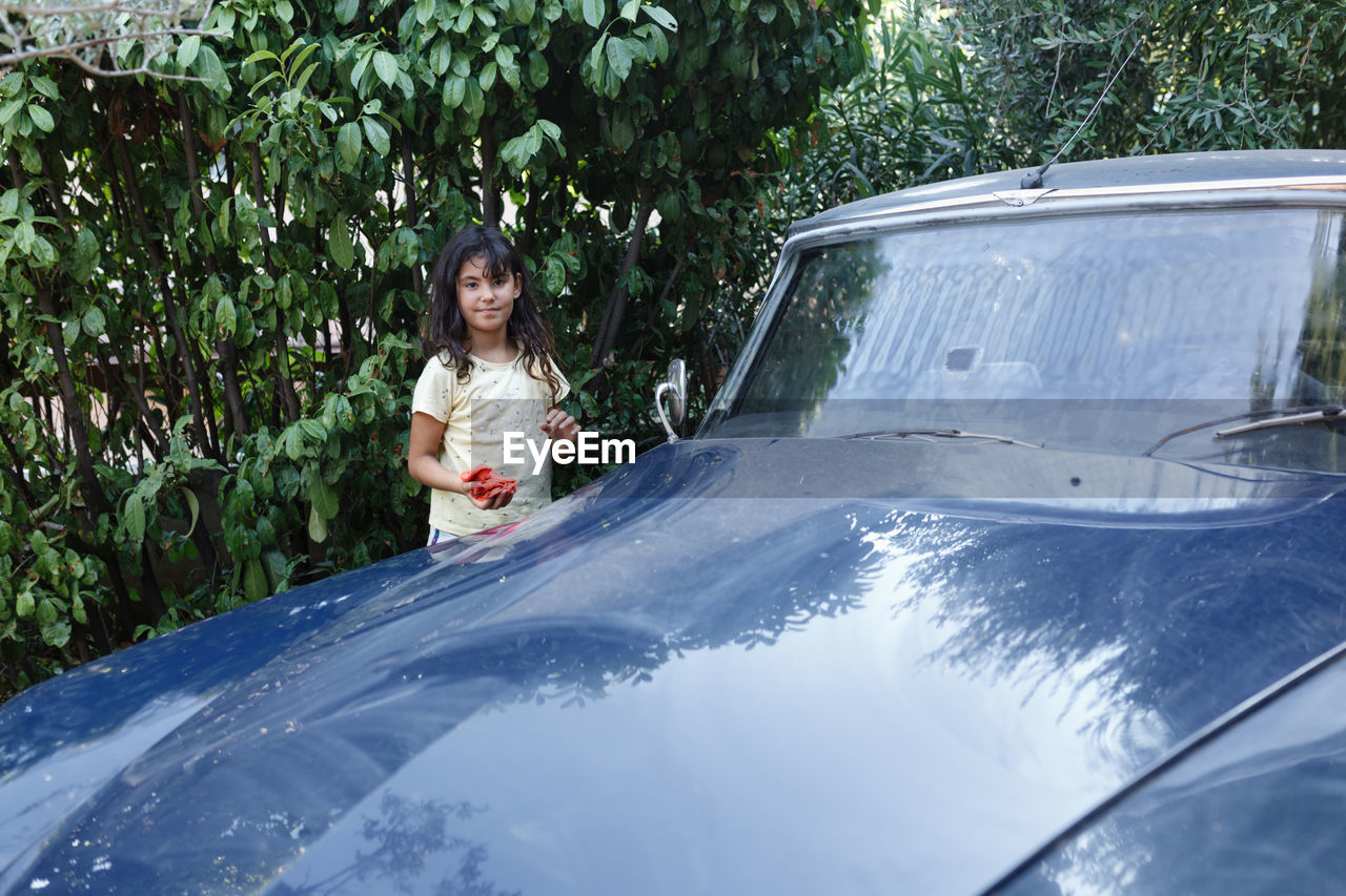Girl watching next to blue car in the garden