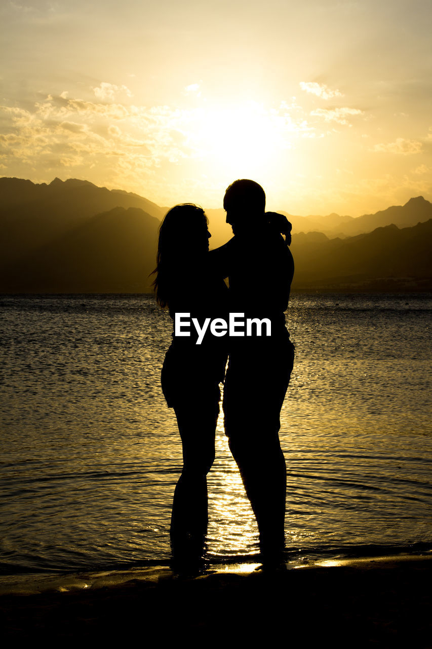 Silhouette romantic couple standing at beach during sunset