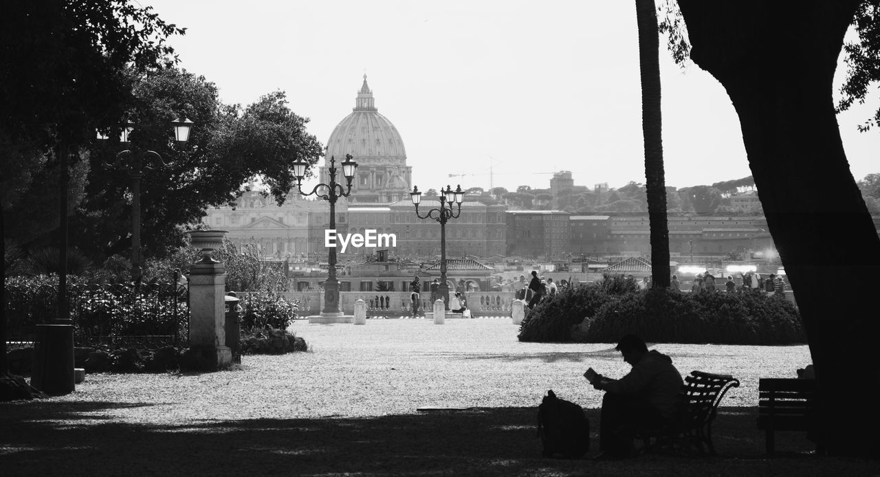 Man sitting on bench at park against historical building