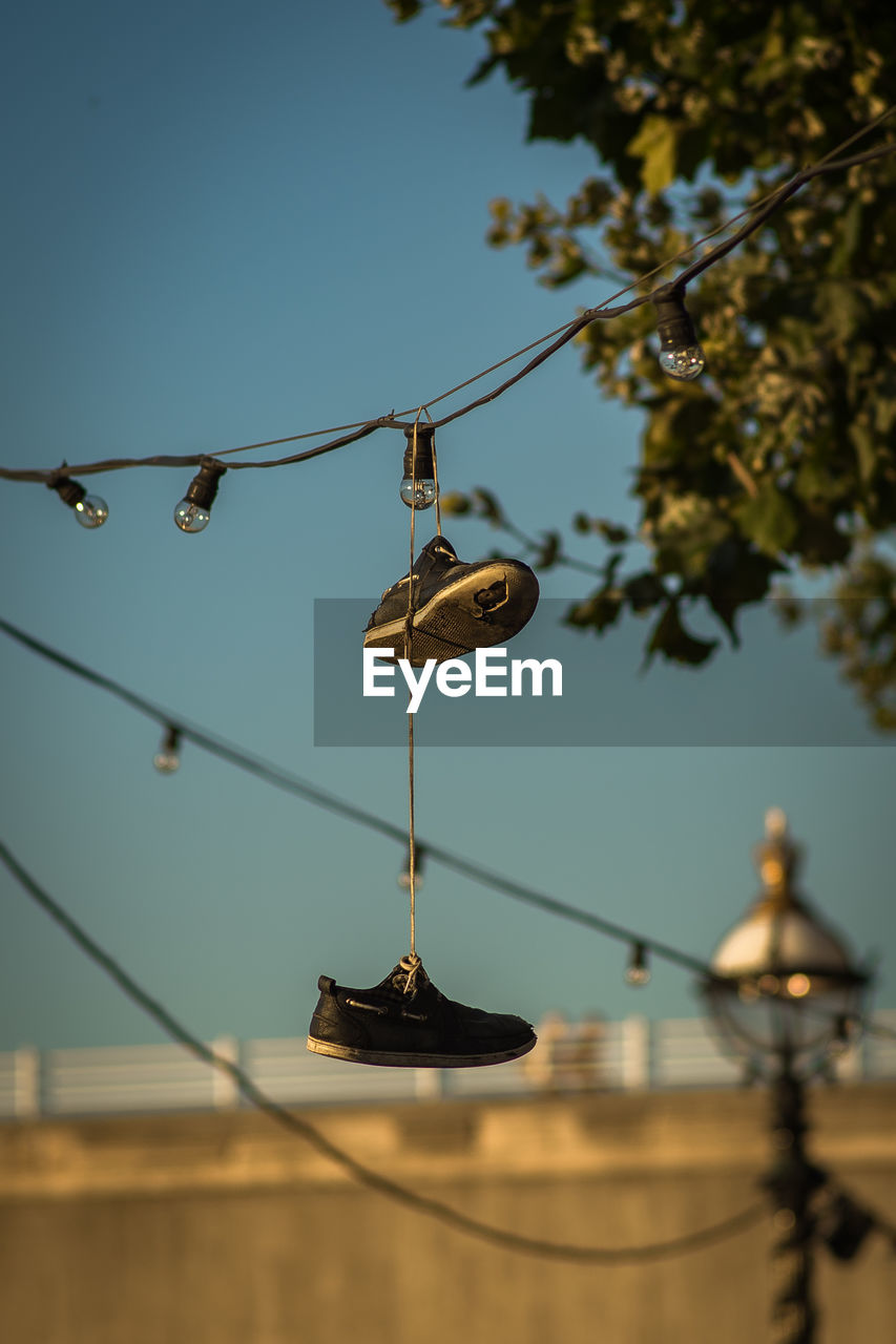 Low angle view of shoes hanging on cable against sky