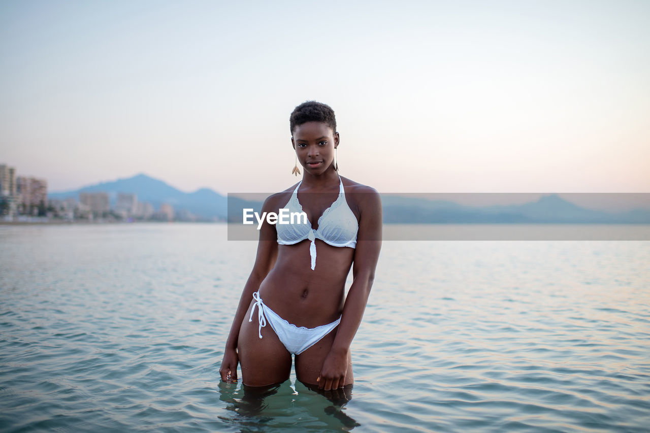 African american female in sea water looking at camera on background of sunset sky