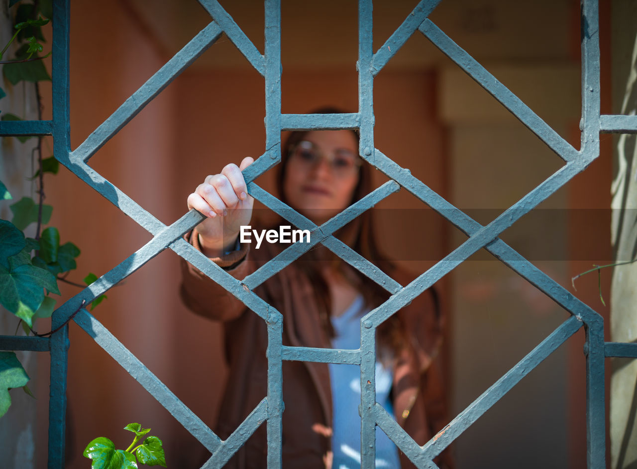 Portrait of woman looking through metal grate