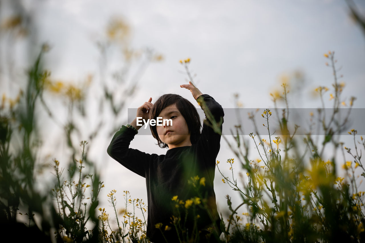 Low angle view on standing girl between yellow flowers with raised arms