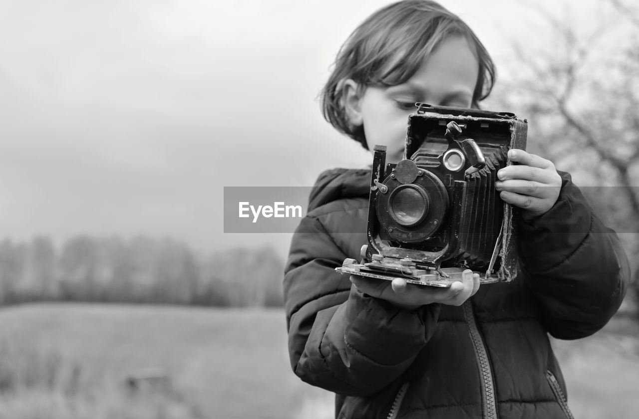 Girl holding vintage camera against sky