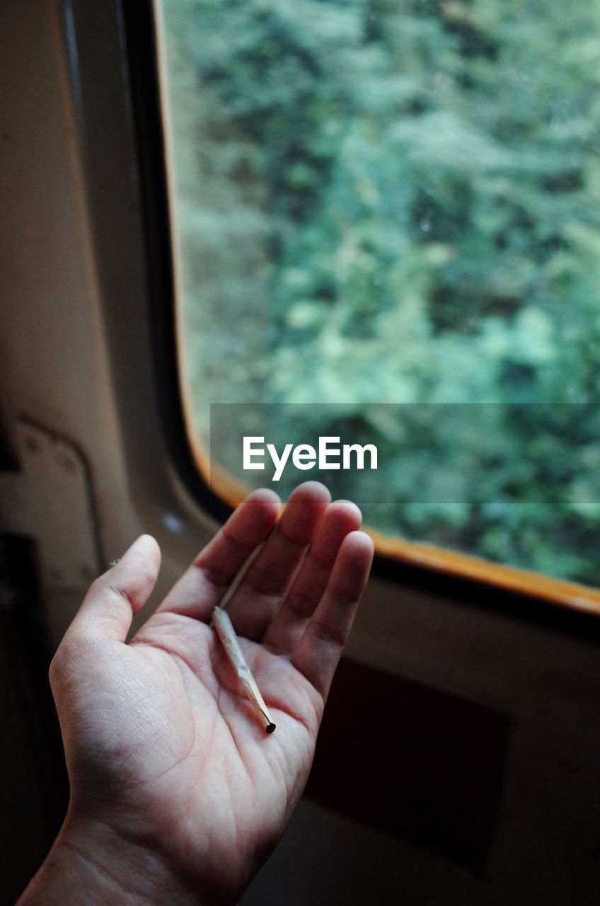Cropped image of hand holding cigarette in train
