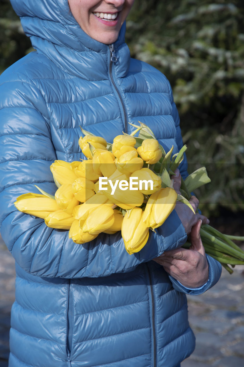 Woman in a blue jacket with a bouquet of yellow spring tulips, mother's day gift