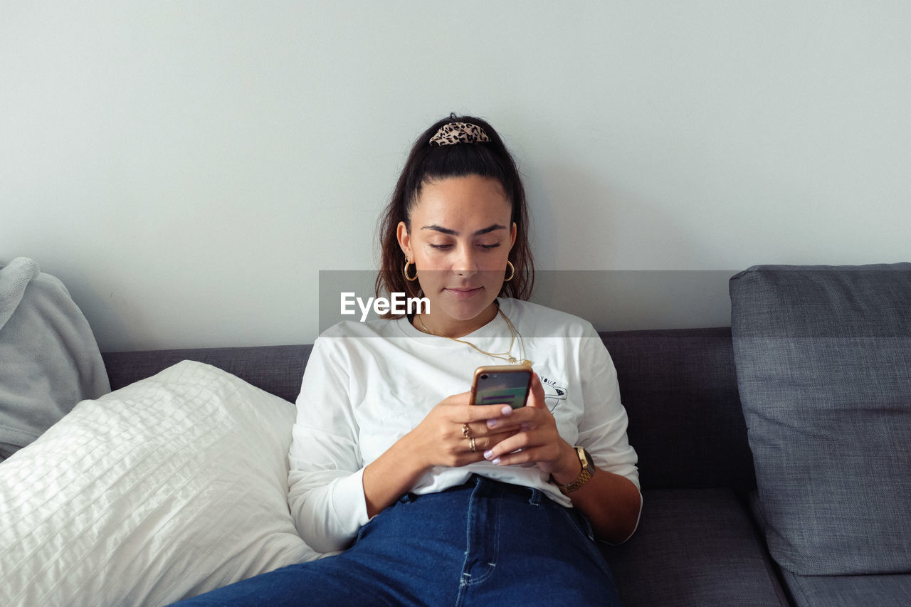 Young woman using mobile phone while sitting on sofa at home