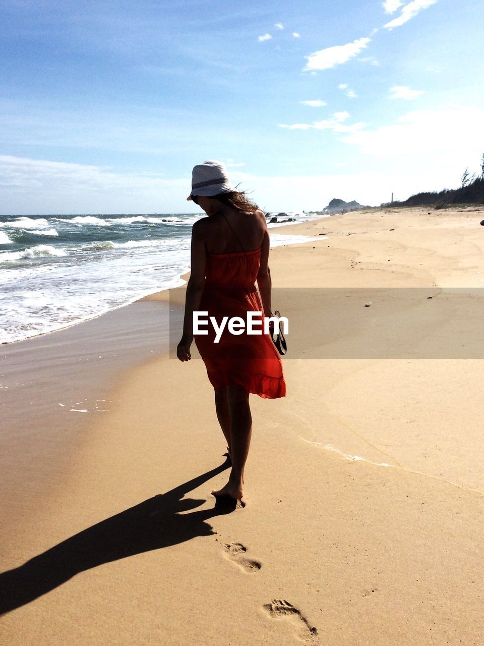 Full length rear view of woman walking at beach against sky