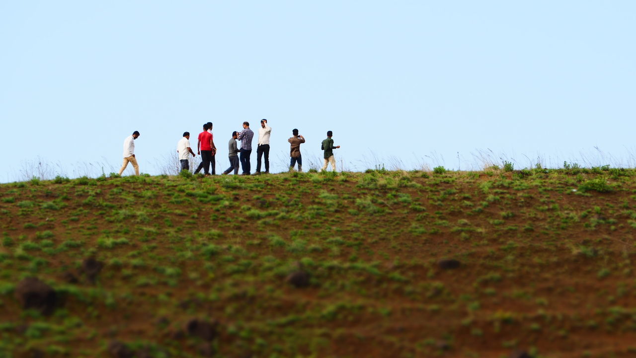 GROUP OF PEOPLE WALKING ON FIELD AGAINST CLEAR SKY