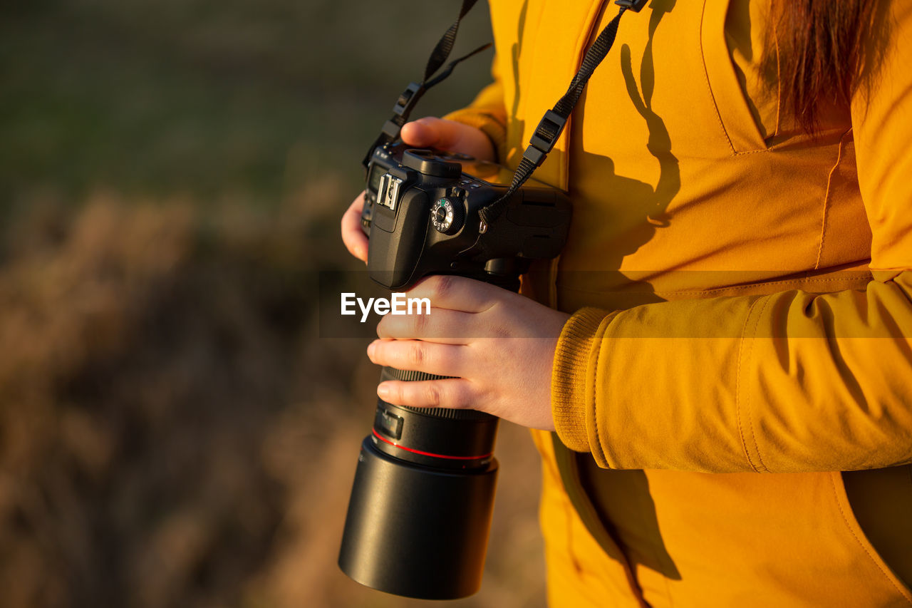 Midsection of woman holding camera standing outdoors