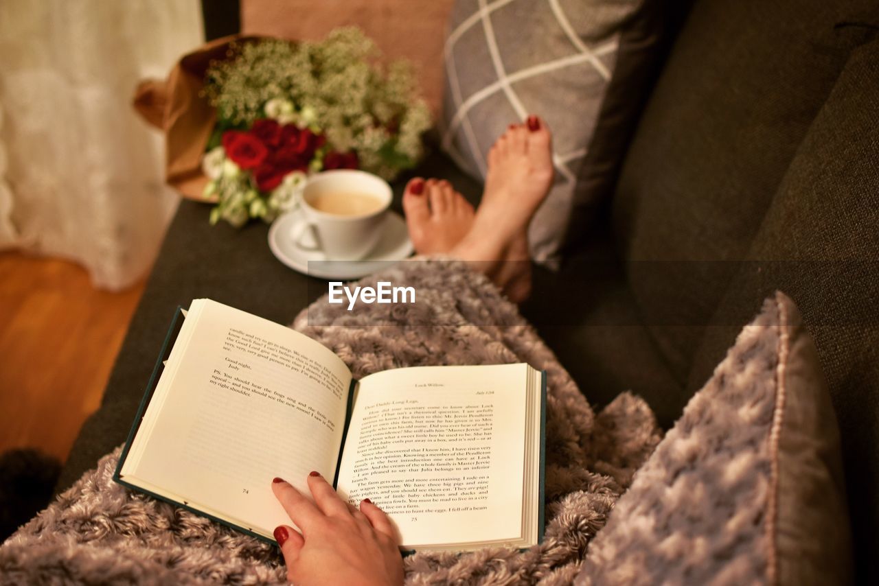 Low section of woman reading book at home