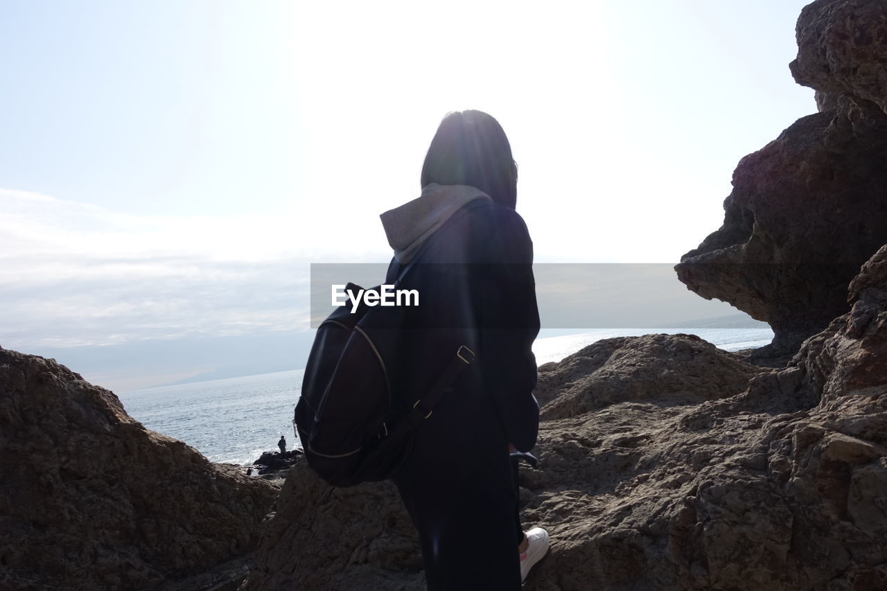 Rear view of woman standing on cliff while looking at sea