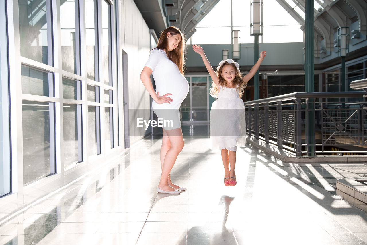 Portrait of happy daughter jumping by pregnant mother at corridor