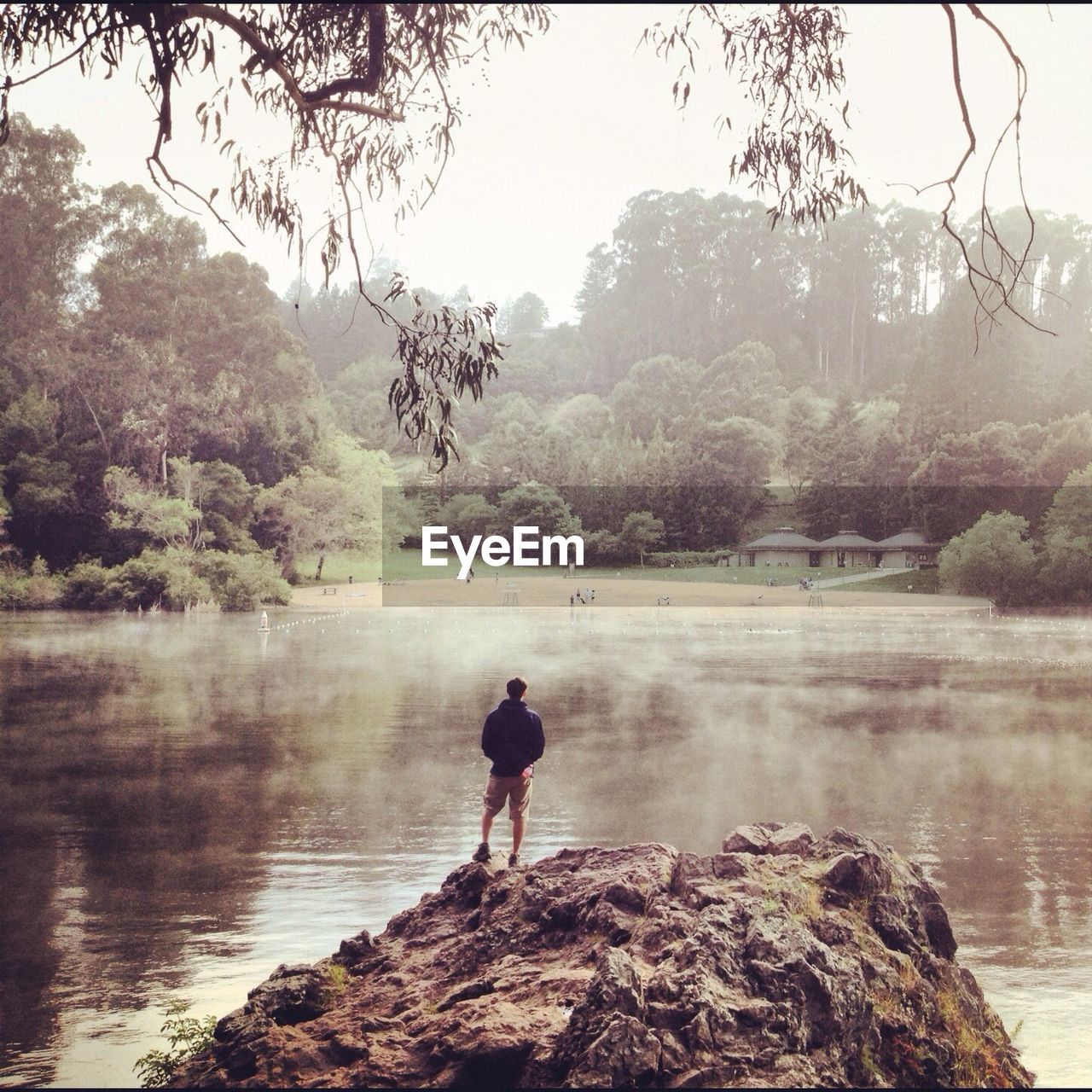 Man standing on rock overlooking countryside lake