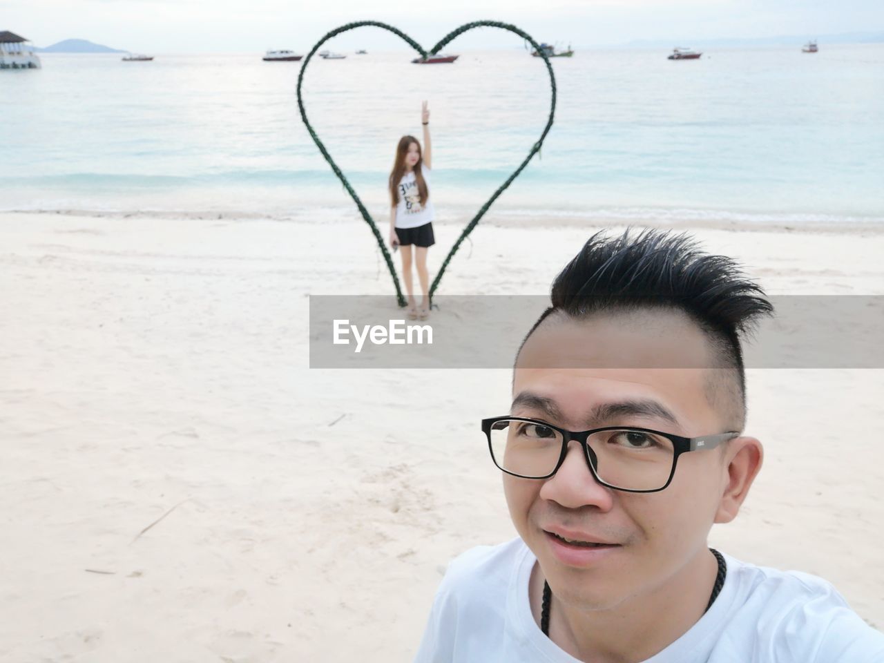 Portrait of man with girlfriend standing amidst heart shape at beach