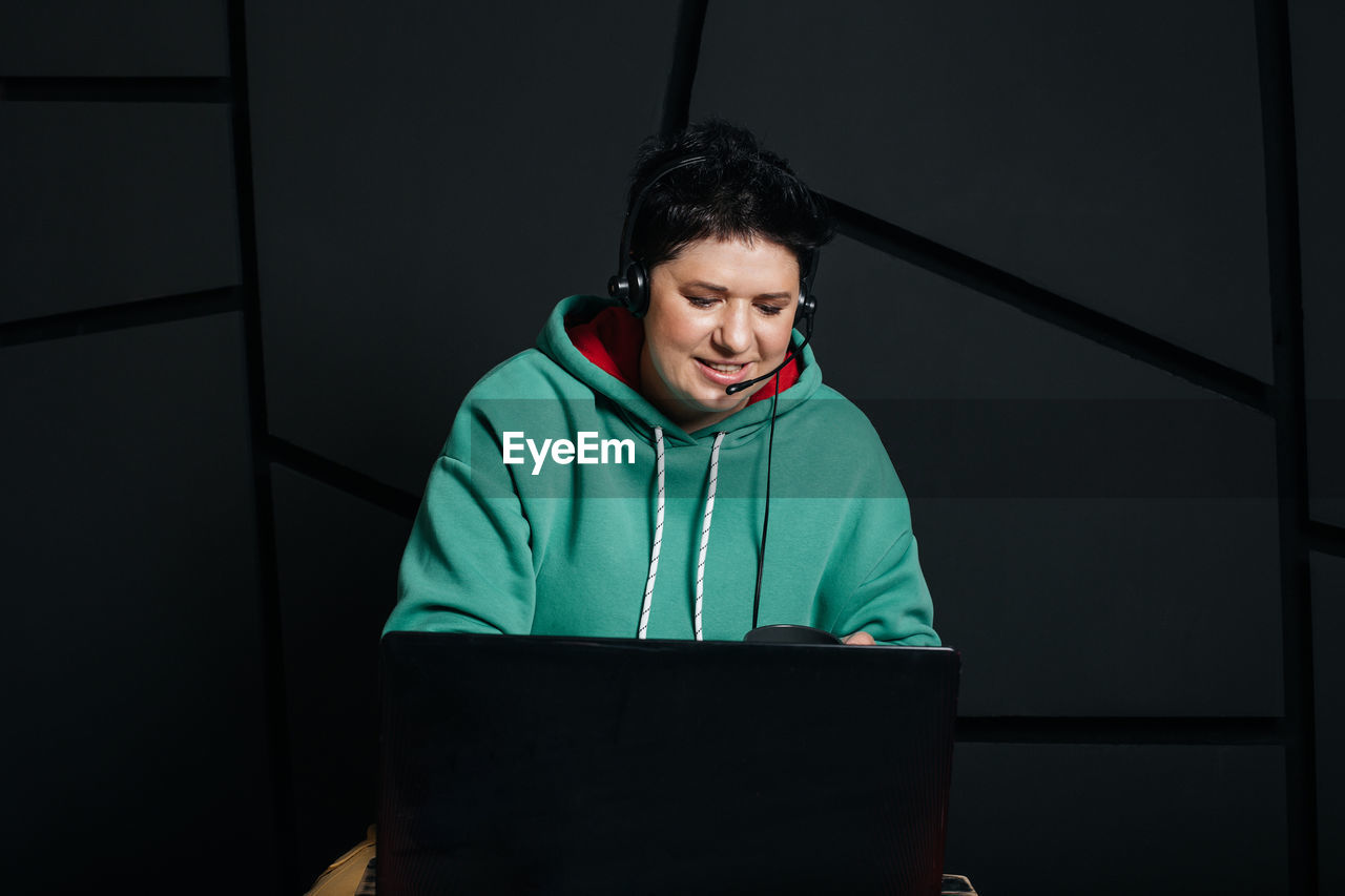 PORTRAIT OF SMILING YOUNG MAN STANDING BY LAPTOP