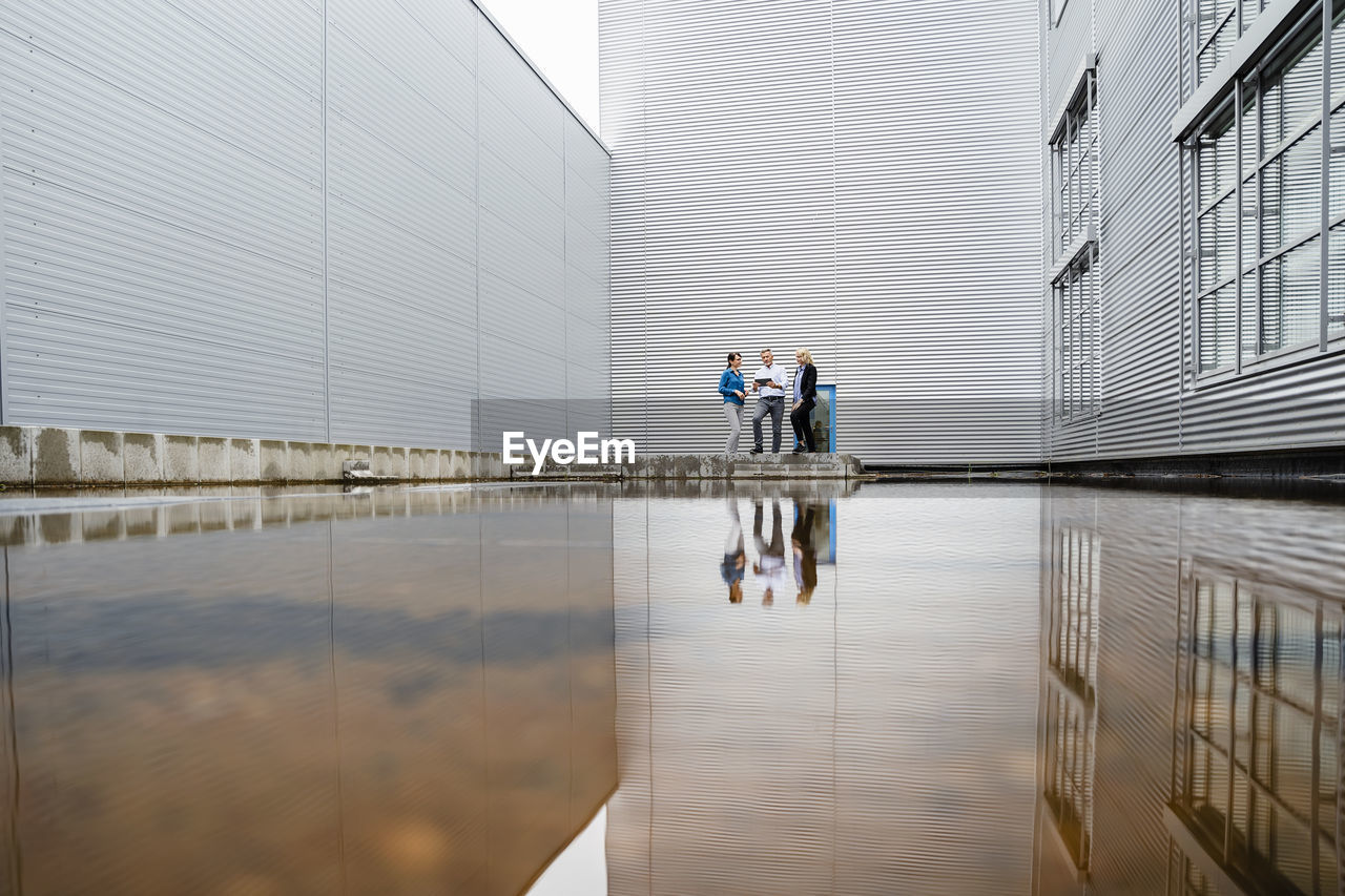 Coworkers with reflection on water in front of industrial building