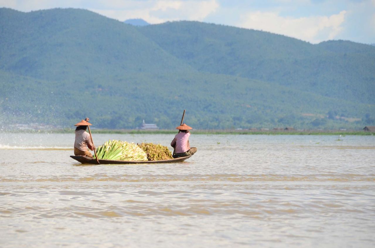 People with spring onions in boat on lake against mountains