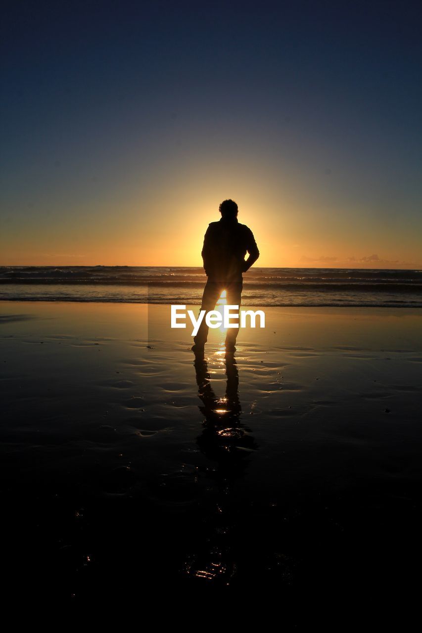 Silhouette man standing at beach against clear sky during sunset