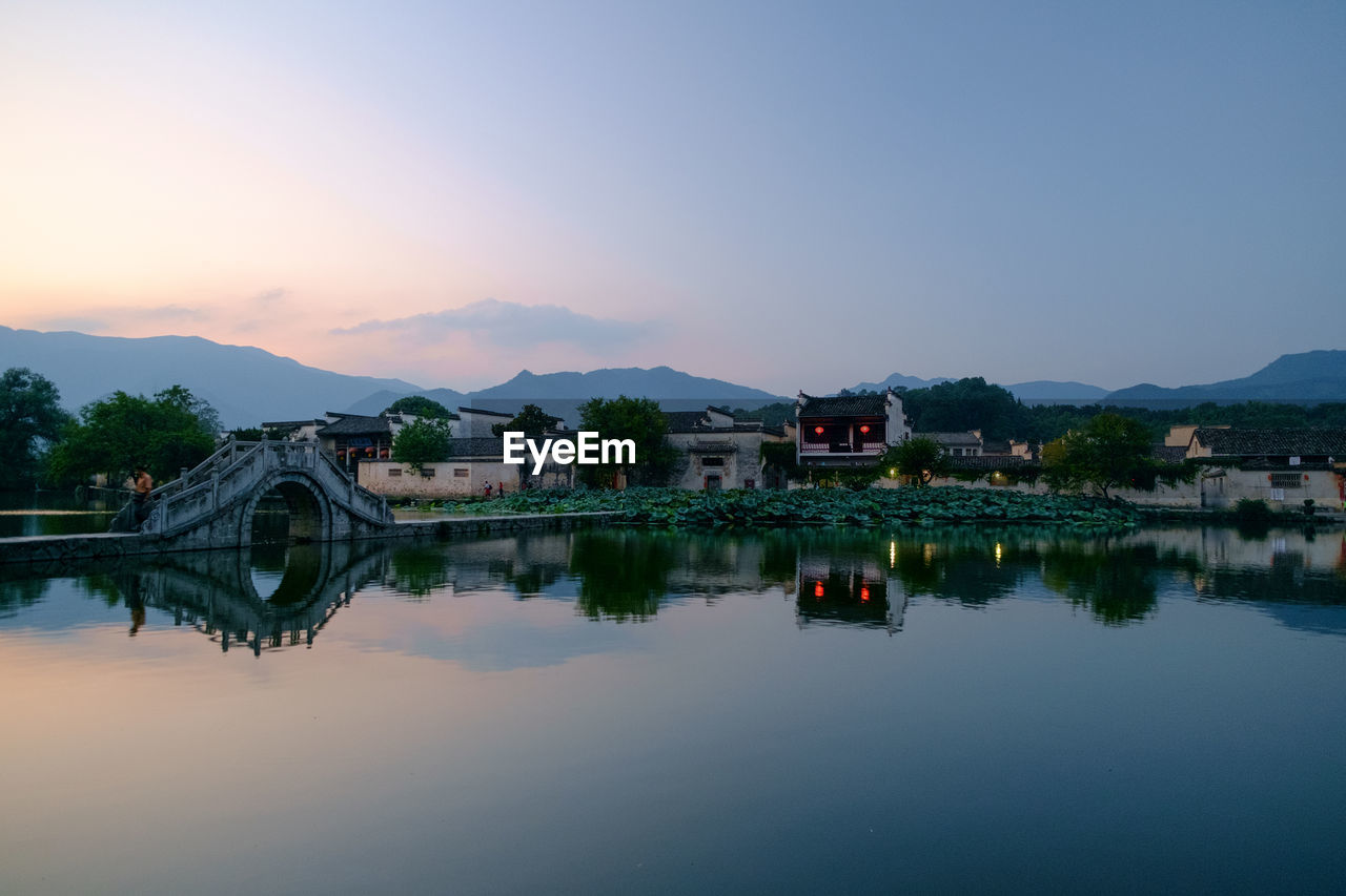 Arch bridge over river by buildings against sky during sunset