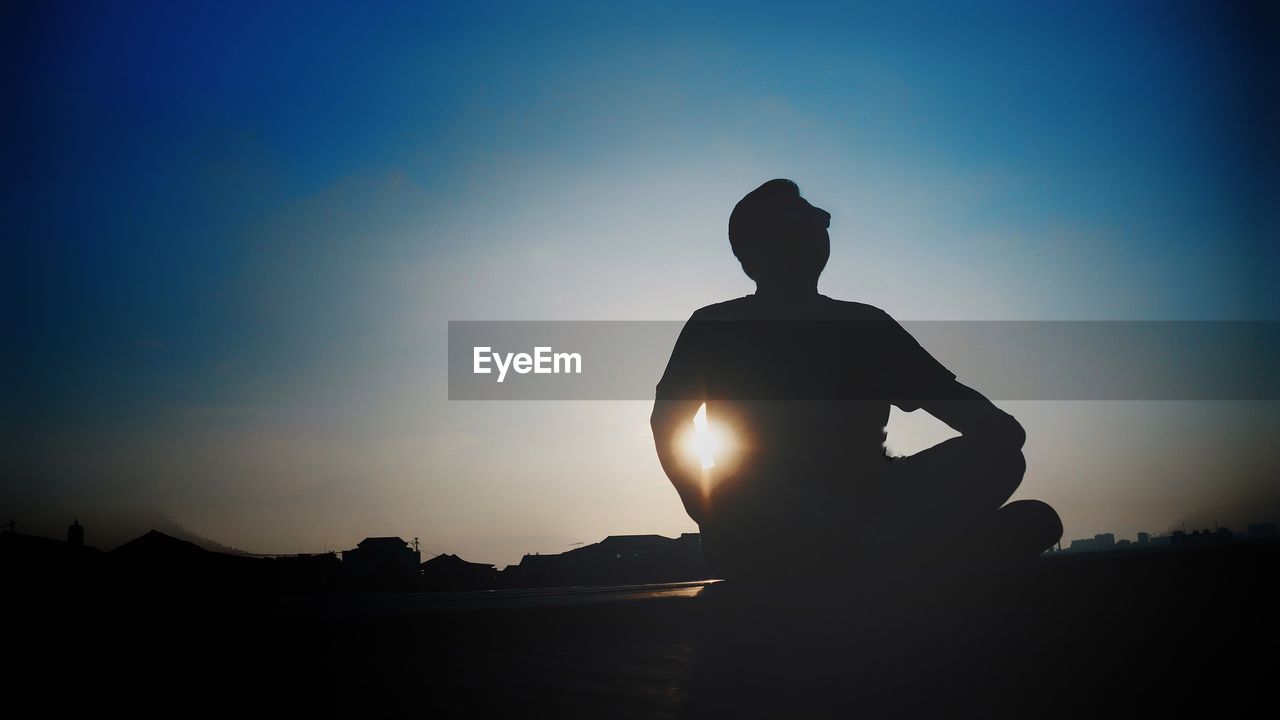 Silhouette man sitting against sky during sunset