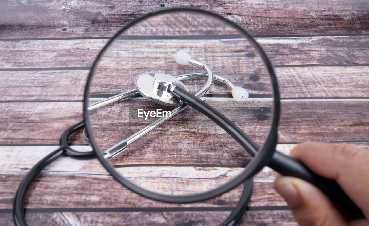 Close-up of hand holding magnifying glass against stethoscope on table