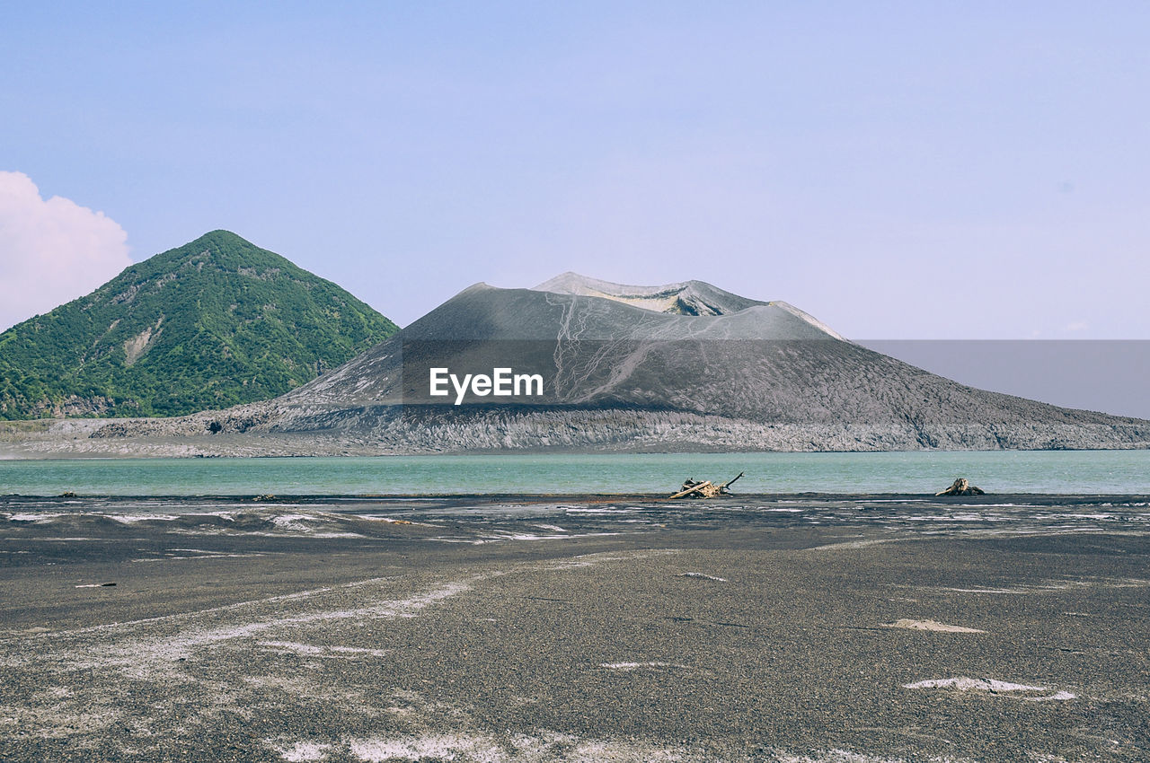 Scenic view of volcano by river against sky