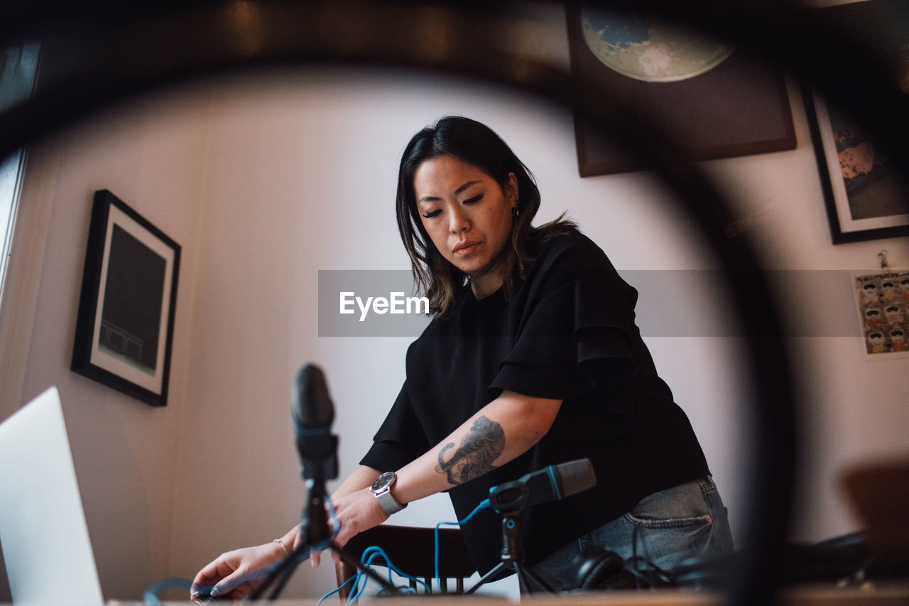 Low angle view of female podcaster standing by microphones on table at home