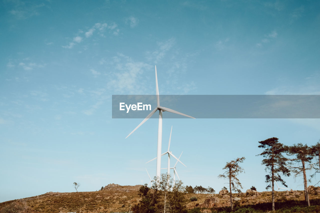 Low angle view of windmills on landscape against sky