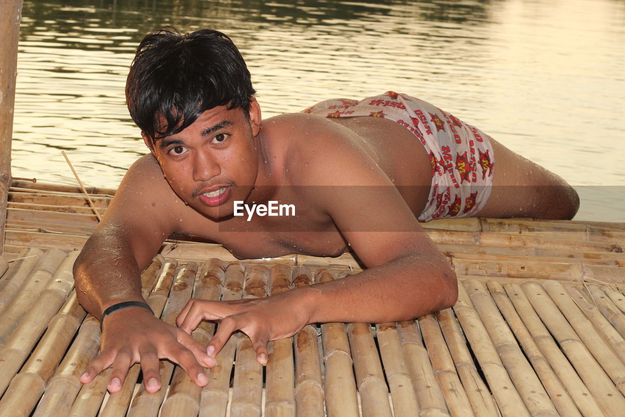 PORTRAIT OF SHIRTLESS YOUNG MAN AT LAKESHORE