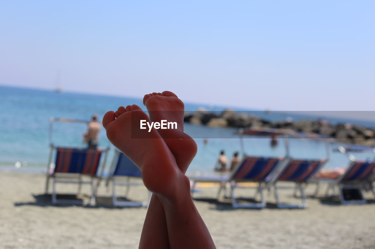 Low section of person at beach against clear sky