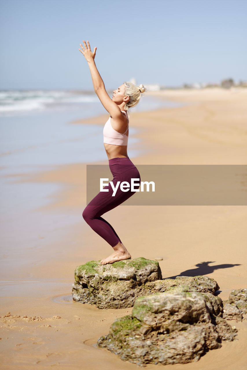 Side view full length of young woman exercising at beach