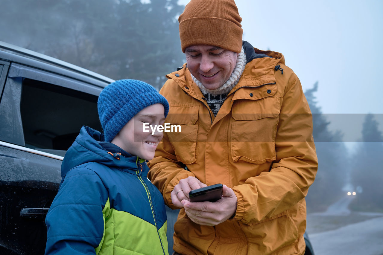 Happy father and son sitting together in car. family in road trip child look pictures on smartphone