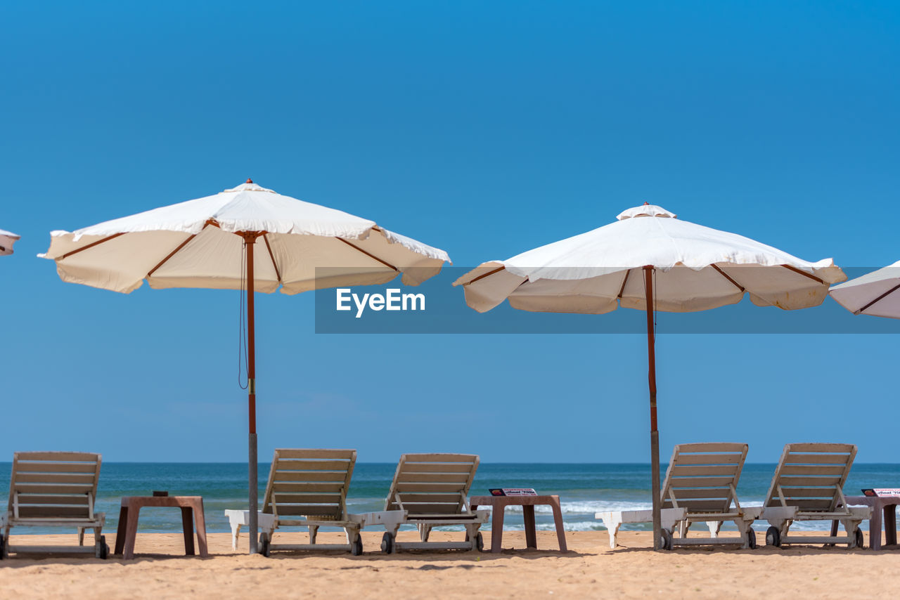 LOUNGE CHAIRS AND TABLES ON BEACH AGAINST CLEAR BLUE SKY