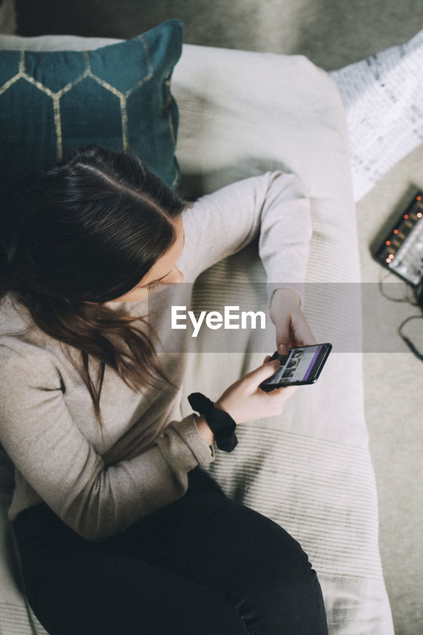 High angle view of teenage girl using mobile phone while lying on bed at home