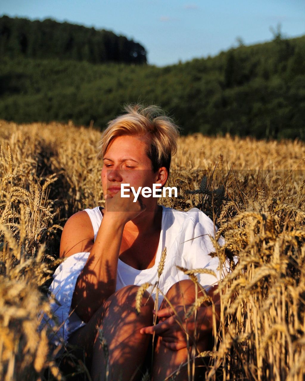 Young woman sitting on field against sky