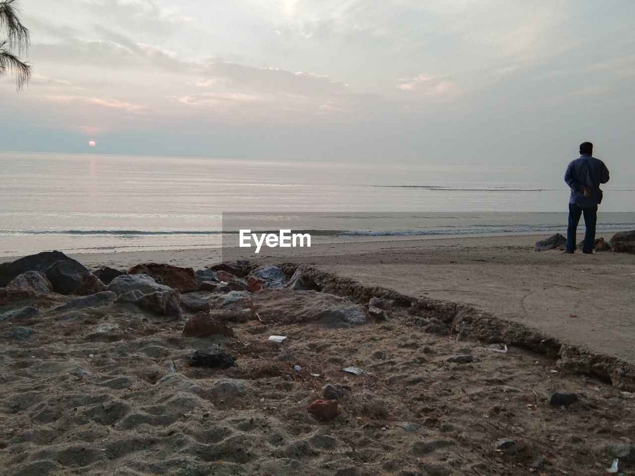 REAR VIEW OF MEN ON BEACH AGAINST SKY DURING SUNSET