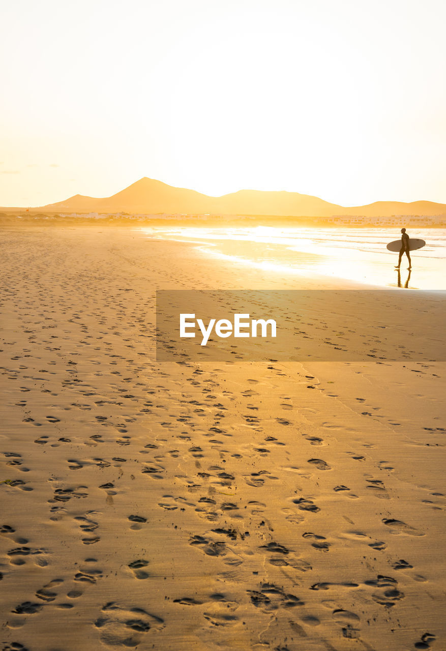 rear view of man walking on beach against sky during sunset